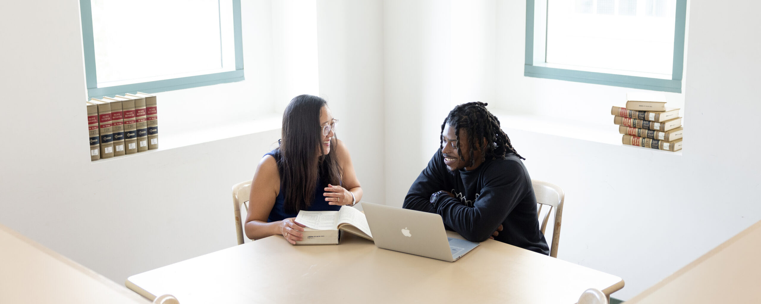Asian female professor working with a Black male student in a library on a college campus.